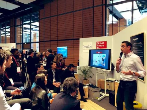 IA, transformation digitale, co-working - super héros de l’entreprise du futur Un homme présente un discours devant une foule attentive, illustrant l'engagement et l'interaction du public.