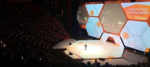 IA, transformation digitale, co-working - super héros de l’entreprise du futur Scène spacieuse dotée d'un grand écran, avec des spectateurs, témoignant d'un événement captivant.